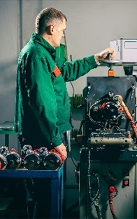 Technik w zielonej kurtce roboczej pracujący przy stanowisku z wieloma turbosprężarkami, wykonujący diagnostykę lub naprawę przy stole warsztatowym